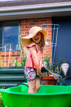 Little girl playing outdoors with hose in backyard wearing big floppy sun hat - water play