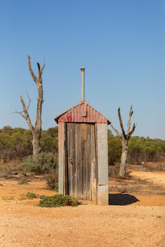 Abandoned outback outhouse in red dirt with blue sky