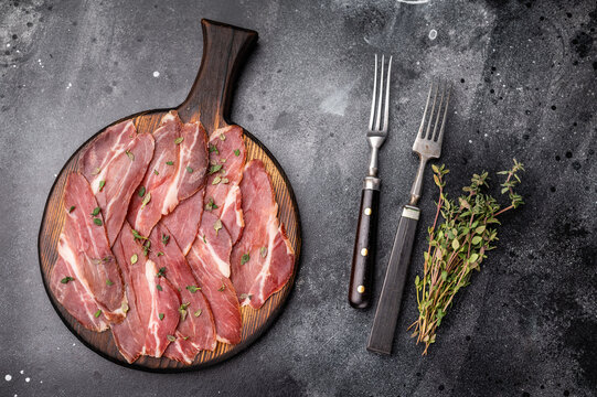 Slovenian ham, sliced cured pork meat on wooden board, Prsut. black background. top view