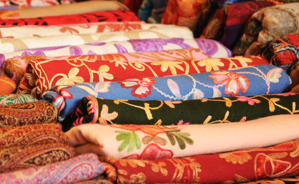 Variety of colorful shawls with floral patterns at street market stall display. Oriental Fashion background..