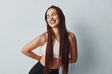 Young woman with long hair in sportswear smiling with eyes closed and hands on back for pain relief...
