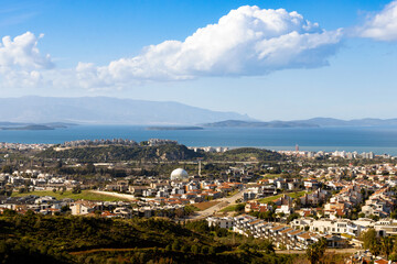 Fototapeta premium Panoramic aerial view of a modern coastal town with luxury villas and houses by the sea, scenic landscape under a blue sky with white clouds. Izmir, Turkey.