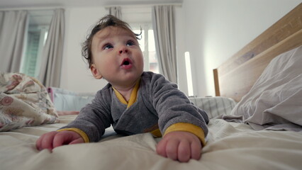 Fototapeta premium Baby lying on stomach on bed, reaching forward with curious and playful expression, early motor skill development, indoor family setting, exploration and growth in early childhood