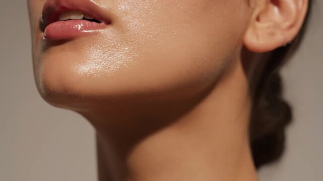 Young woman's face showing perfectly hydrated, dewy skin with glossy lips, emphasizing natural beauty and a radiant glow motion clip.
