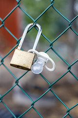 Baby pacifier attached to a brass padlock on a wire fence.
