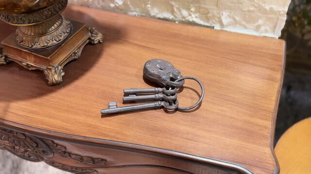 Close-up of antique iron skeleton keys attached to an old padlock resting on a polished wooden table indoors, highlighting vintage craftsmanship and rustic interior decor details.