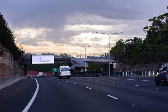 Van driving towards bridge overpass with digital billboard  above road