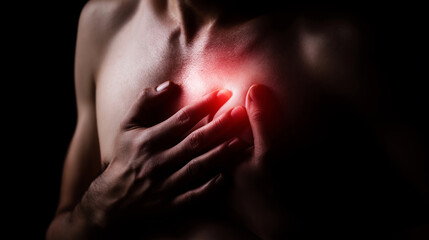 Obraz premium Person clutching chest with both hands, experiencing discomfort or pain in the heart area with a bright red glow