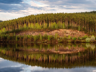 Obraz premium Southern Urals in summer: Bashkortostan, village pond on the Kaga River at sunset, reflection of pine trees in the water.