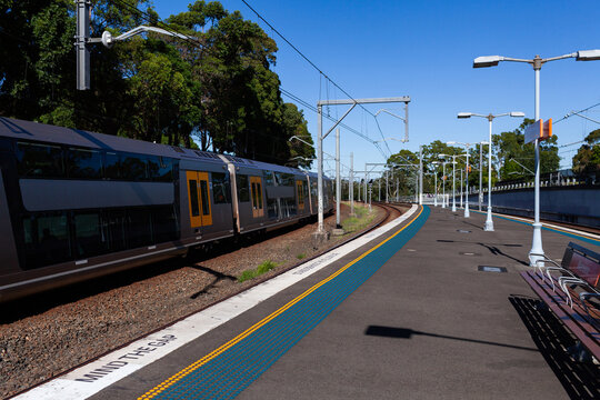 passenger train passing platform of Narwee station in Sydney suburb on bright sunlit day