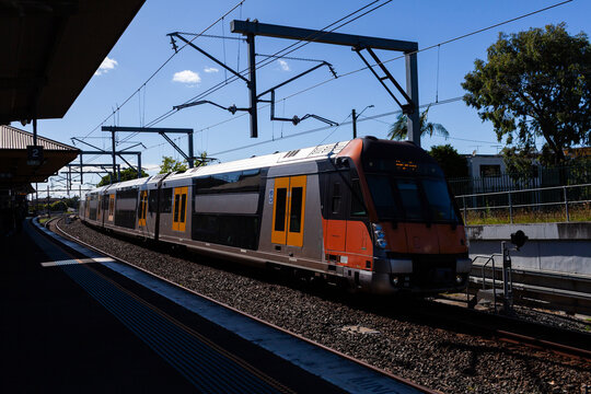 passenger train passing platform of Narwee station in Sydney suburb on bright sunlit day