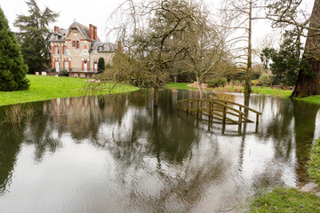 Obraz premium Crue hivernale, parc public avec un étang débordant et une passerelle submergée devant une belle maison. Parc de la Morinière, Rezé