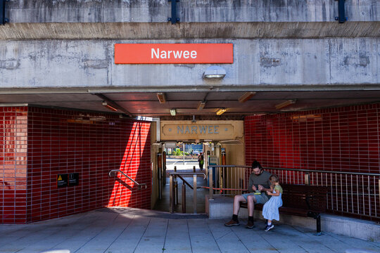 Narwee train station sign with old sign in tunnel to train station with people seated on bench