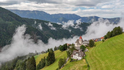Aerial drone view of village, town Eores (Afers) near Bressanone (Brixen). Cloudy summer day. View on the Church of San Giorgio in the centre. Idyllic mountain village in the Italian Dolomites.