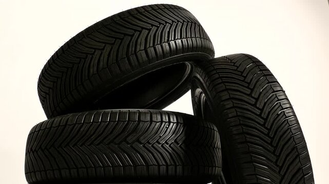A close-up studio shot of a stack of new, black car tires with visible tread patterns, ready for automotive use and maintenance.
