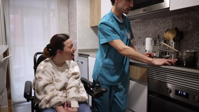 Kind male caregiver in scrubs helping a smiling young woman in a wheelchair with meal preparation at home, showing support, assistance, and inclusion for people with physical disabilities