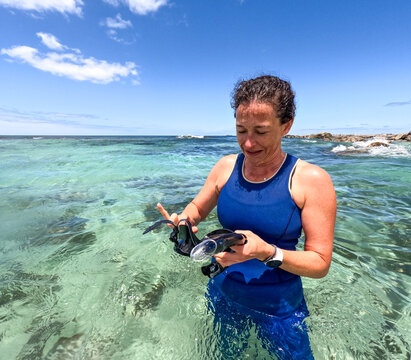 Woman snorkelling in clear blue green water adjusting snorkel and mask with sun shining