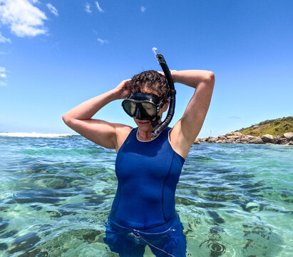 Woman snorkelling in clear blue green water adjusting snorkel and mask with sun shining