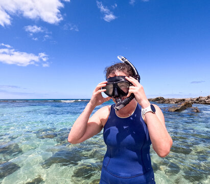 Woman snorkelling in clear blue green water adjusting snorkel and mask with sun shining