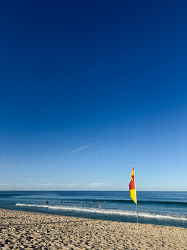 Surf lifesaving beach red and yellow flag  with small waves and swimmers in background