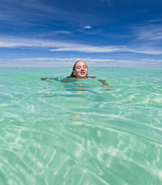 Young girls head above water swimming in clear green ocean with bright blue sky