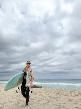 Woman holding mid length surfboard on overcast beach background