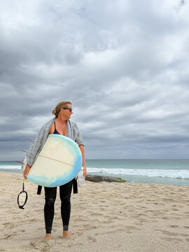 Woman holding mid length surfboard on overcast beach background