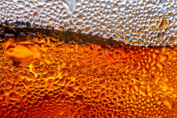 Macro Abstract of Cold Amber Liquid with Water Condensation Droplets,A high-angle, macro shot focusing on the golden-amber hues of a chilled beverage inside a glass. The surface is covered. © banjongseal324