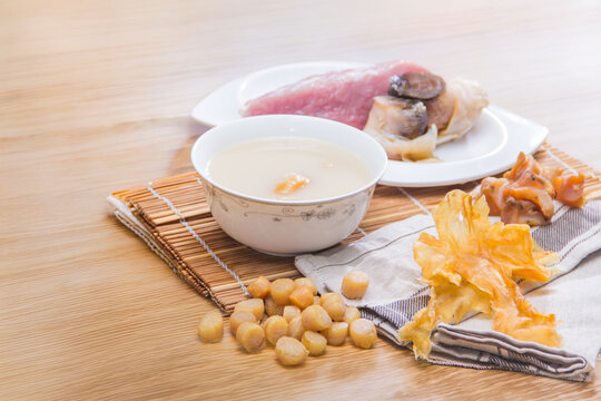 A white porcelain bowl of creamy congee served with dried scallops, pork slices, and mushrooms on a wooden mat.
