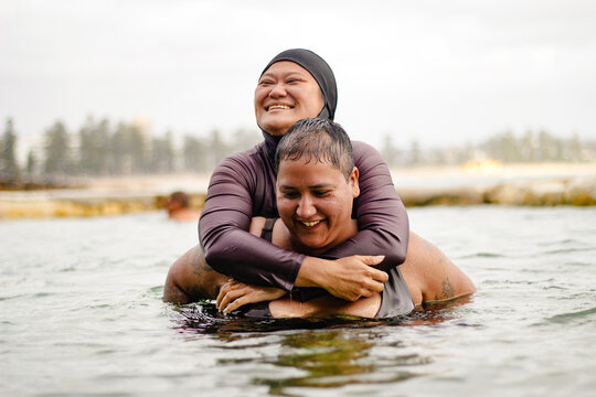 Hmong-American woman riding on piggyback of French Islander woman inside tidal pool