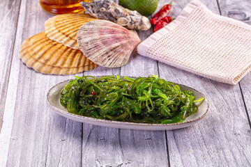 Japanese seaweed salad Chuka with sesame seeds and chili in a white bowl on a wooden table.