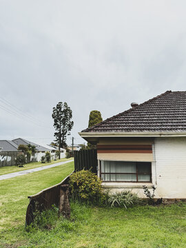 Suburban scene of old weatherboard house with window and aging fence with green grass