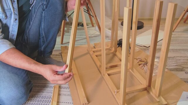 Person building flat-pack wood furniture on a rug, performing diy assembly