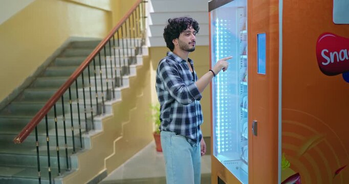 Indian happy young adult gen z smart male man use easy fast self service choose juice drink press button campus area. Lady female walk stairway thirsty boy take bottle enjoy break day time hallway
