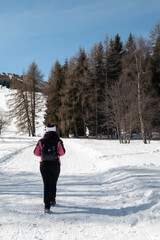 A woman, photographed from behind, is trekking on a snow-capped mountain. The woman has long black hair, wears a black and pink ski jacket and has a white headband on her forehead