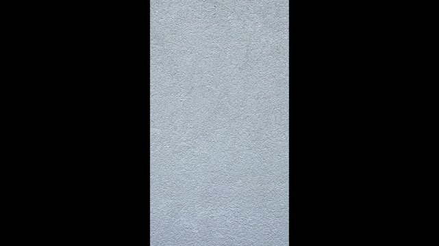Vertical video with a slow downward camera movement along a gray textured wall surface. Minimal background footage highlighting rough plaster texture and neutral tones.
