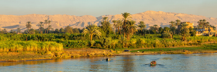 Panoramic landscape of palm trees and fields on the Nile river banks,  egyptian people in rowing boats, Egypt travel header © Delphotostock