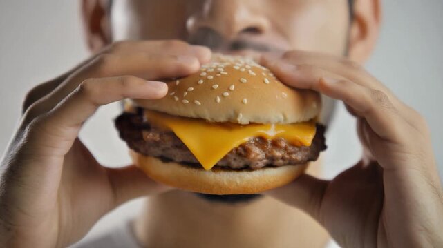 A man holding a cheeseburger in front of his face with both hands, showcasing the burger's details.