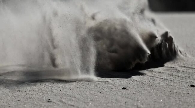Close up of blowing dust and sand on a dry surface. Black and white macro photography of wind sweeping powder or dirt particles. Abstract motion, environment drought, or fast speed concept.