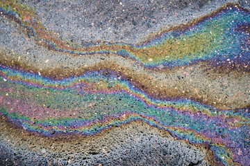 Obraz premium The gasoline or fuel pollution has created a vibrant rainbow pattern on the cracked asphalt surface, resembling an oil slick