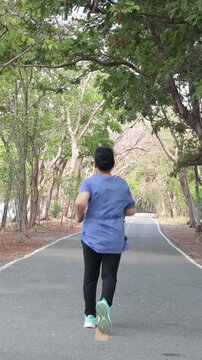 Back view of an elderly Asian woman power walking for exercise in a public park during the morning.