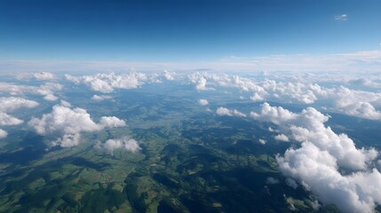Aerial view of a green rolling landscape seen from above clouds under a clear blue sky