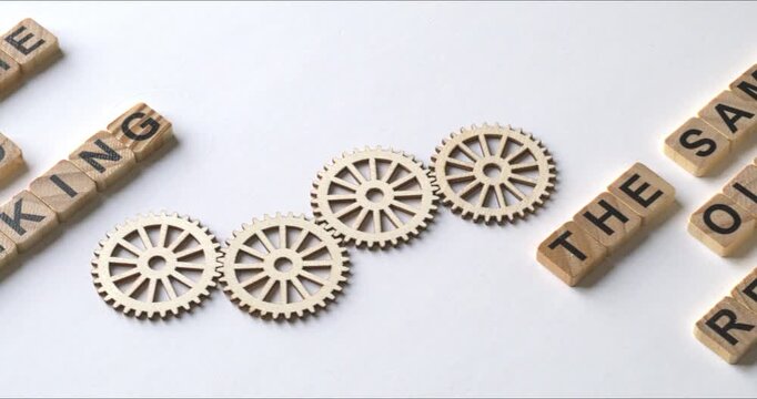 The same old results as a consequence of the same old thinking. Motivational quotes on wooden blocks and gearwheels between them. Camera slide.