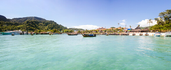 Wide view of Tonsai Bay on Koh Phi Phi Don, Phi Phi Island, Thailand. In the foreground, numerous traditional Thai long-tail boats are anchored in the shallow, pale turquoise water of the harbor.  © Stefano Tammaro