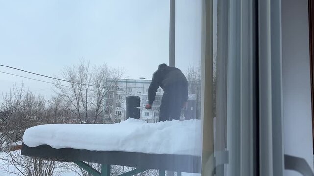 Unrecognizable worker removing snow from the roof of an apartment building with shovel.