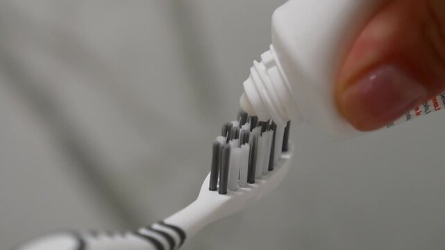 Woman's hand applying toothpaste to toothbrush, close-up of oral care routine, healthy smile.