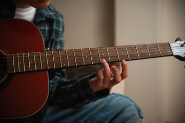 Fototapeta premium Teenage Boy Strumming Acoustic Guitar While Practicing Music In Cozy Home Interior