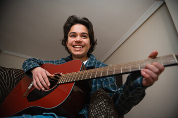 Obraz premium Teenage Boy Playing Acoustic Guitar at Home, Smiling While Strumming and Learning Music