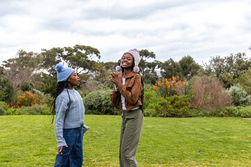 Fototapeta premium Two African American teenage female friends standing on park lawn wearing knit pom-pom beanies