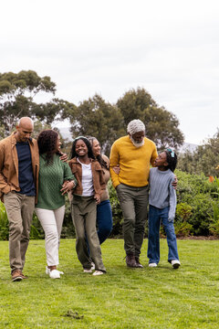 African American family with senior, teenage and child walking across lawn in park wearing sweaters